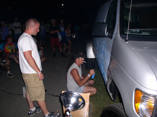 Man spray painting a van's side panel. Other people watch in the background
