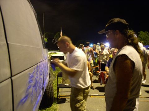 1978 Ford Mustang II - A person is airbrushing flames onto the side of a white van at an outdoor event at night.