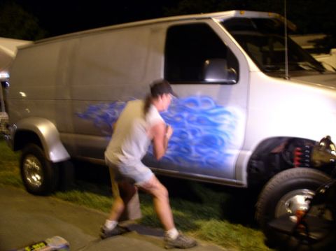 1978 Ford Mustang II - A person stands next to a silver van with custom blue flame airbrushing on its side.