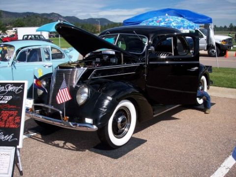 1972 Ford Ranchero - A black 1937 Ford sedan is displayed with its hood open, parked next to a light blue car at an outdoor event.