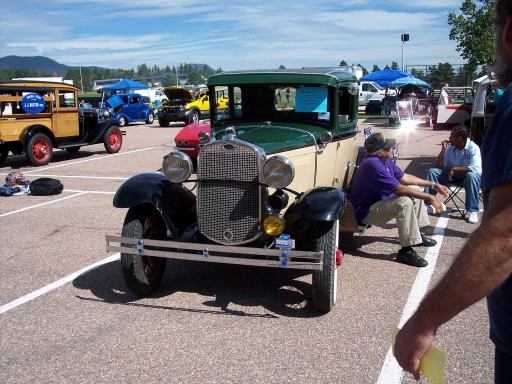 Green and cream Ford Model A sedan at an outdoor car show, front three-quarter