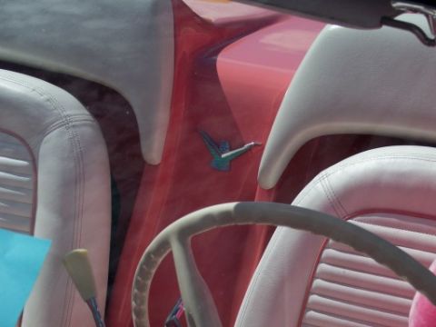 1972 Ford Ranchero - A turquoise bird emblem is visible on the red dashboard between the white seats of this classic car interior.