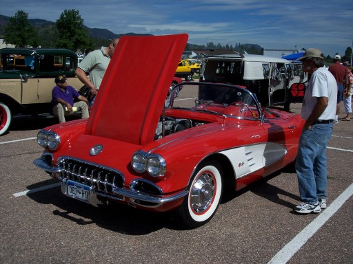 Red 1950s Chevrolet Corvette roadster with hood open at a car show, front three-quarter