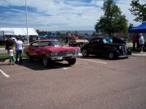 1972 Ford Ranchero - A red 1968 Chevrolet Chevelle is parked next to a black classic car under a blue tent.