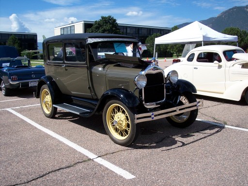 Olive-green Ford Model A Tudor sedan with gold wire wheels at a car show