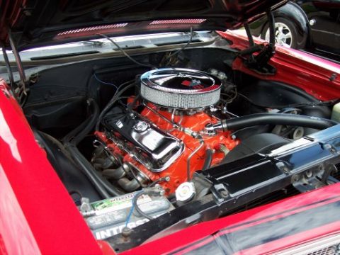 1972 Ford Ranchero - The engine bay of a red vehicle is shown, a chrome air cleaner and an orange engine block. A portion of another vehicle is visible in the b…