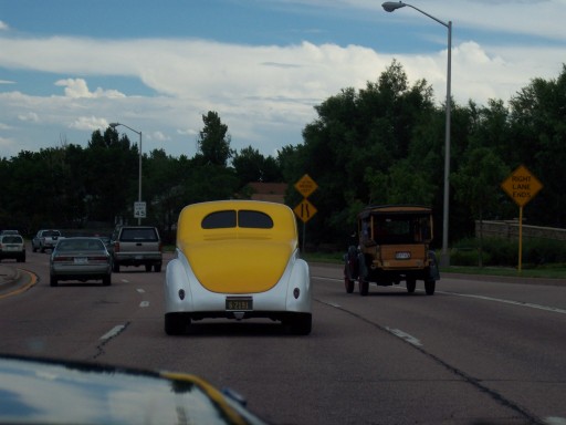 Yellow and white 1930s hot rod coupe and a yellow open-cab truck driving on a highway