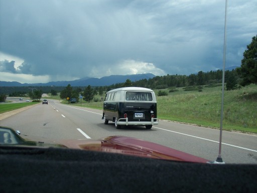 VW bus, black over white, seen ahead on a highway from a following car's windshield.