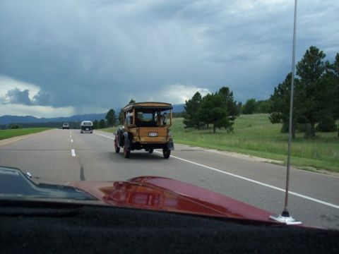 1972 Ford Ranchero - A vintage wooden car travels down a highway under a cloudy sky, with other vehicles in the distance.