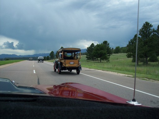 Antique yellow touring car ahead on a rural highway under storm clouds