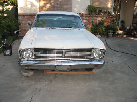 1966 Ford Ranchero - A white 1964 Ford Falcon is shown from the front, parked on a cracked concrete driveway with plants in the background.