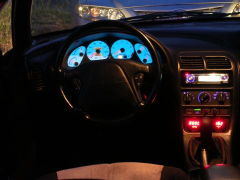 1996 Ford Probe - Interior view of a car at night, illuminated blue gauges and a custom stereo system, with another vehicle's headlights in the background.