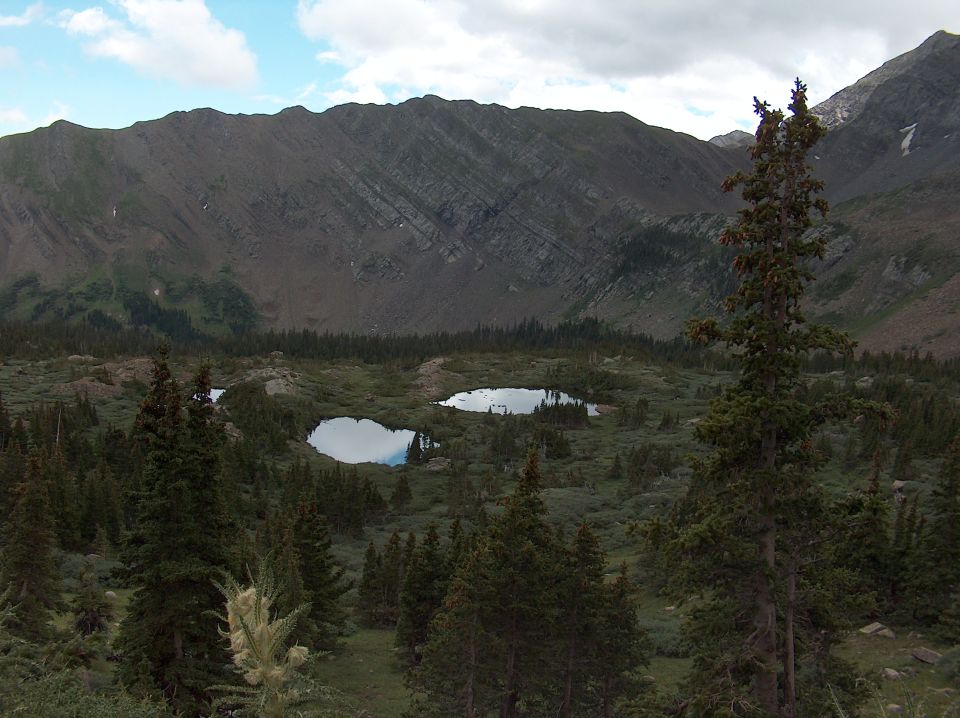 Mountain range overlooks two small lakes surrounded by pine trees and scrub brush