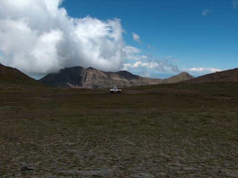 1978 Ford Bronco - A white pickup truck is parked in a vast, rocky landscape under a cloudy sky with mountains in the distance.