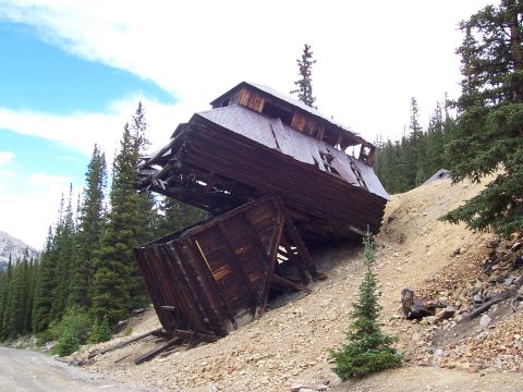 1991 Ford Bronco - An old, decaying wooden structure leans precariously on a mountainside, surrounded by evergreen trees.