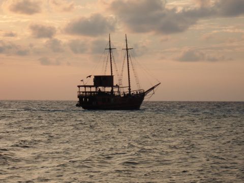 1991 Ford Bronco - A two-masted sailing ship is silhouetted against a cloudy sunset sky over the ocean.