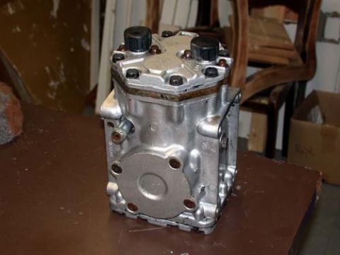 1996 Ford Bronco - Cleaned and freshly painted silver York-style piston compressor standing on a brown workbench, showing the round bolt-on end cover, black s…