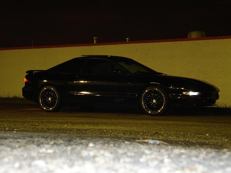 Black coupe in profile at night with rear spoiler and chrome lace-spoke wheels