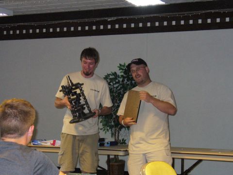 1991 Ford Probe - Two men are presenting engine components at an event, with a third person visible in the foreground.