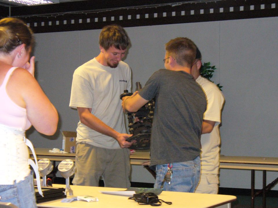 Engine part held by two men, with a woman in the foreground