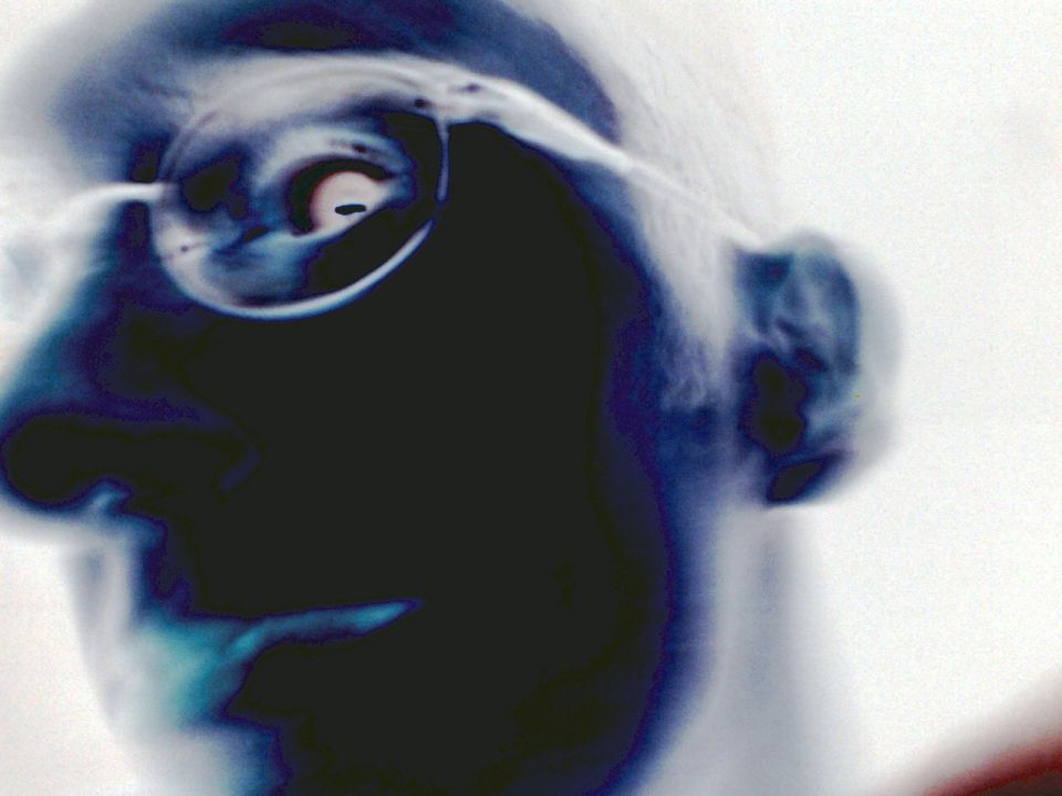 Close-up of a person's face in profile, wearing glasses. The image is inverted