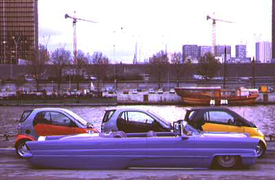 1972 Ford Ranchero - A purple convertible and two Smart cars are parked along a waterfront with city buildings and cranes visible.