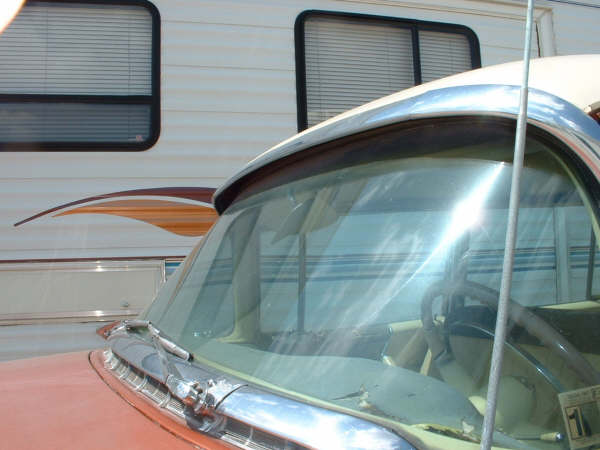 Front of a car with a large windshield, next to an RV. Steering wheel visible inside the car