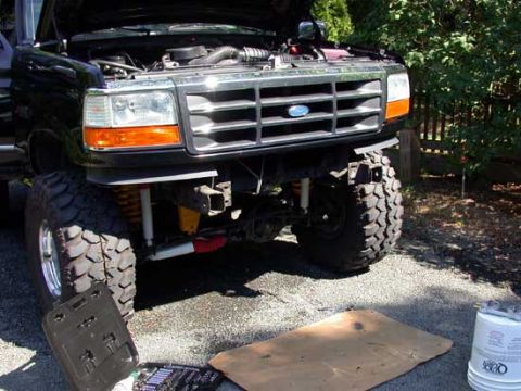 1996 Ford Bronco - Front view of a black lifted Ford Bronco with the hood up and front bumper removed, exposing the chrome grille, radiator support, coil spri…