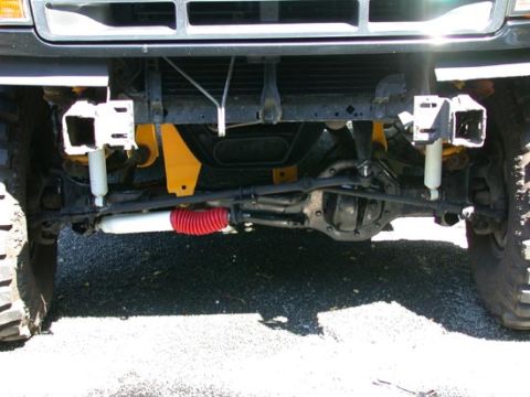 1996 Ford Bronco - Low front view under a lifted Ford truck's front end on asphalt, showing the Twin Traction Beam front suspension with a differential housin…