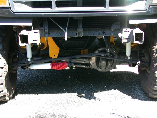 Underside of lifted Ford front suspension: TTB axle, white shocks, red steering stabilizer
