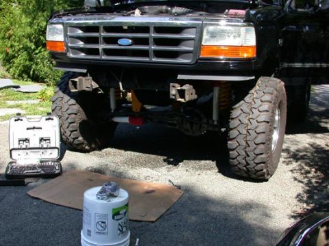 1996 Ford Bronco - Low front view of a lifted black Ford truck on aggressive mud-terrain tires and chrome wheels, with amber corner lenses and a chrome grille…