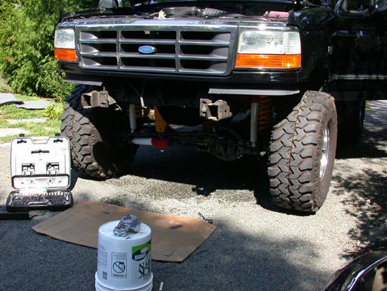 Lifted black Ford truck front end on mud tires with tools laid out on driveway
