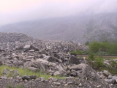 1995 Ford Bronco - A large rock slide covers a hillside, with trees and a railroad track visible in the distance under a hazy sky.
