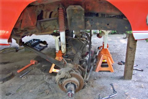 1978 Ford Bronco - The underside of a vehicle is shown on jack stands, with suspension and drivetrain parts exposed for maintenance.