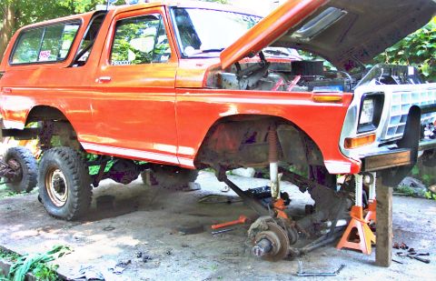 1978 Ford Bronco - This orange SUV is raised on jack stands with its hood open, indicating it is being worked on.