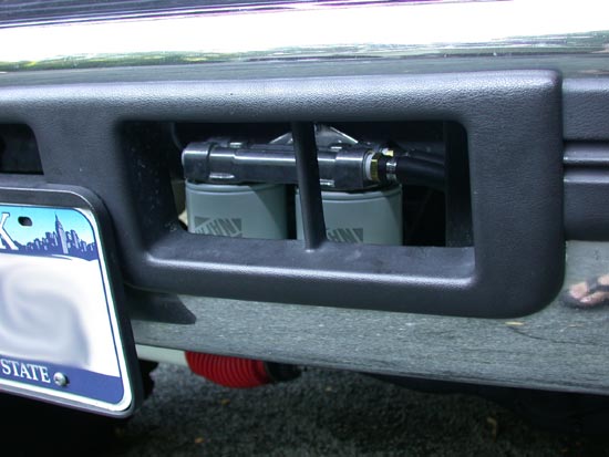 Dual fuel filters mounted inside a black bumper opening near a partial license plate