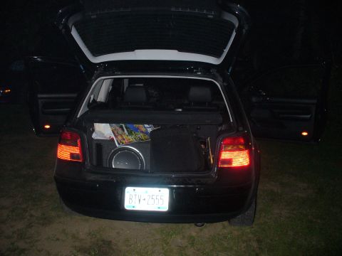 1991 Ford Probe - Rear view of a black hatchback with its trunk open, revealing a subwoofer and other items inside.