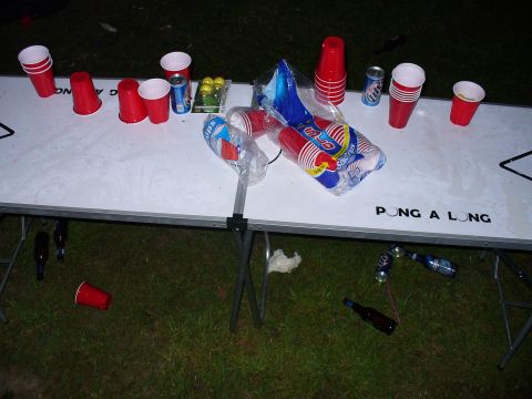 1991 Ford Probe - A beer pong table is set up on the grass with cups, cans, and ping pong balls scattered around.