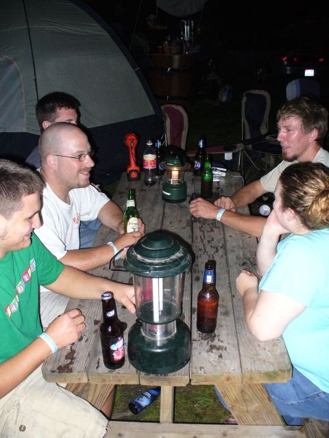 1991 Ford Probe - Friends gather around a wooden picnic table at night, illuminated by lanterns and surrounded by beer bottles.