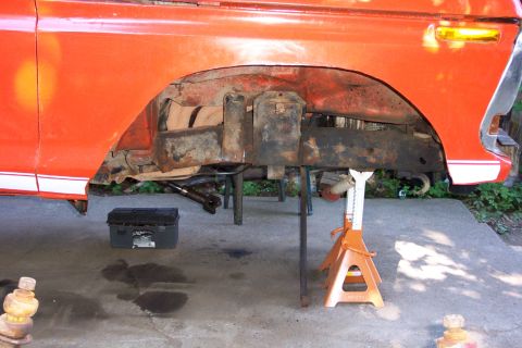 1978 Ford Bronco - The vehicle's undercarriage is visible, supported by jack stands, with significant rust on the frame.