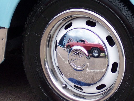 Chrome hubcap on a blue vehicle reflects a red 1972 Ford Ranchero with its hood up