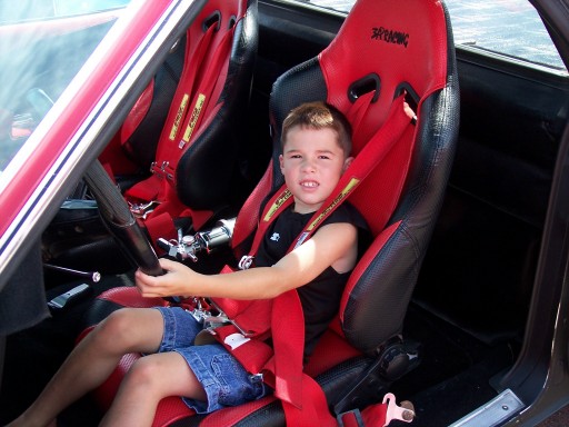 Child sits in a red racing seat with a roll cage visible