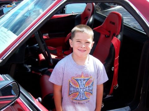 1972 Ford Ranchero - A young boy stands in the interior of a red car with custom racing seats at a car show.