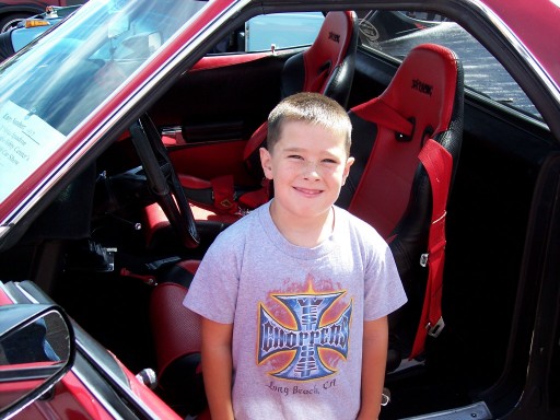 Boy standing in open door of a red car with red and black racing bucket seats