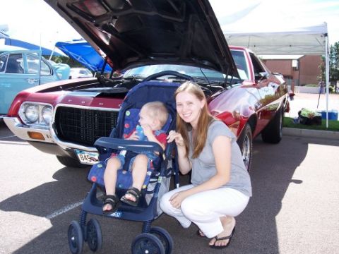 1972 Ford Ranchero - A red Ford Ranchero is displayed at a car show with its hood open, while a woman and child pose nearby.