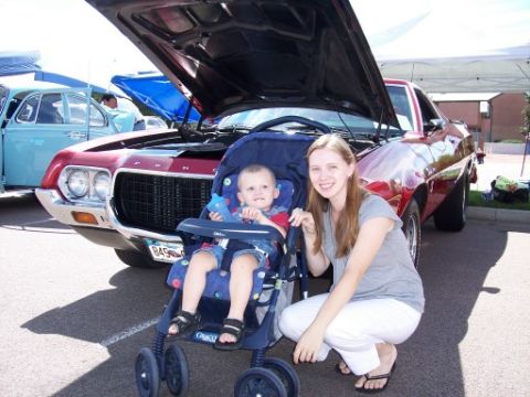 1972 Ford Ranchero - A red 1972 Ford Ranchero is displayed at a car show with its hood open, while a woman and child pose in front of it.