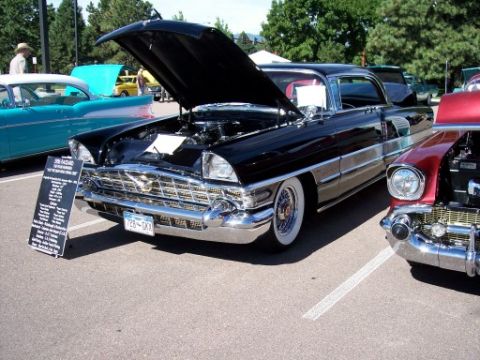 1972 Ford Ranchero - Black 1956 Cadillac Coupe de Ville at a car show, hood open, with other vehicles nearby.