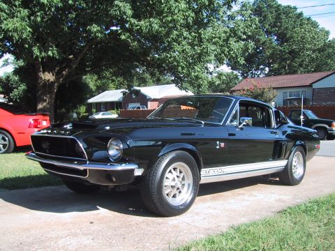 1968 Shelby GT500 - A black 1968 Shelby GT500 coupe is parked on a driveway, with other vehicles visible in the background.