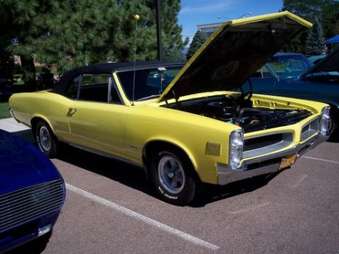 1972 Ford Ranchero - A yellow convertible is parked at an outdoor event with its hood open, showing the engine bay.