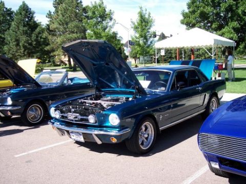 1972 Ford Ranchero - A dark teal 1965 Ford Mustang coupe is displayed with its hood and trunk open at a car show, alongside other vehicles.
